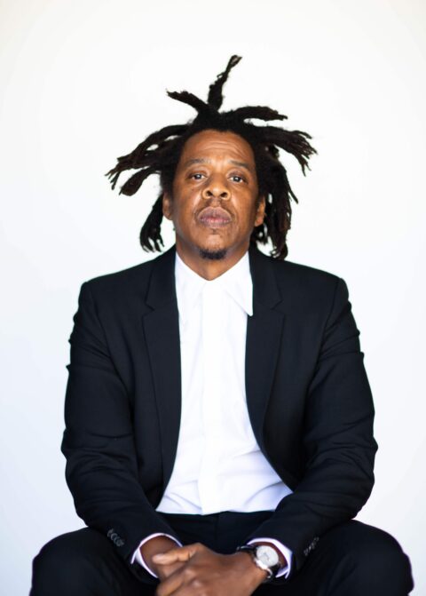 A black and white photo of D’USSÉ founder, JAŸ-Z, looking intently into the camera, while wearing a dark suit and white-collared shirt.